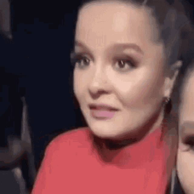 a woman in a red sweater is sitting next to another woman in a dark room .