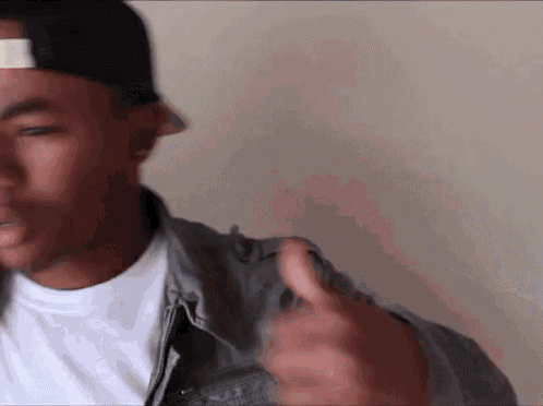 a man wearing a baseball cap and a denim jacket is giving a thumbs up