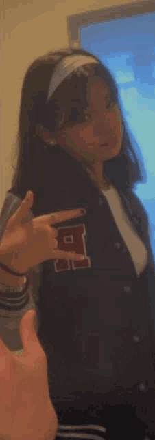 a girl wearing a varsity jacket and a headband is taking a picture of herself in a mirror .