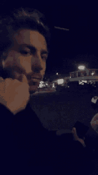 a man is standing in a parking lot at night looking at his phone