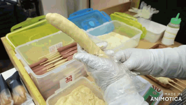 a person wearing gloves is holding a bread stick in front of containers that say made in animatica