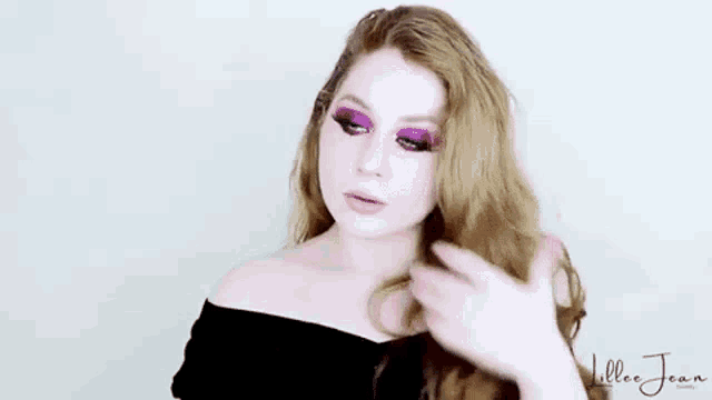 a woman wearing purple eye shadow and a black off the shoulder top is holding her hair .