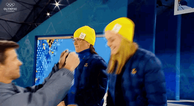 a man is taking a picture of a woman wearing a yellow hat with the word olympic channel on the bottom