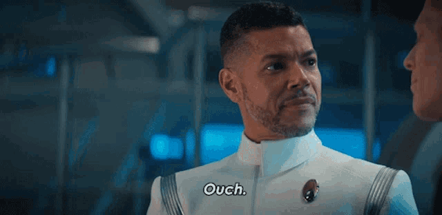 a man in a white uniform is talking to another man and says ouch