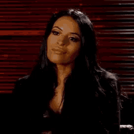 a woman with long black hair is sitting in a chair in front of a red blind .
