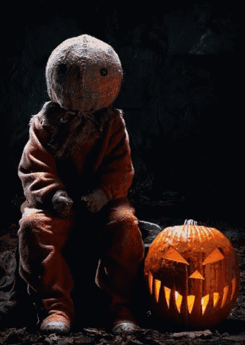 a scarecrow sitting next to a carved pumpkin with teeth