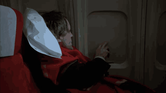 a man is laying on an airplane with a red blanket
