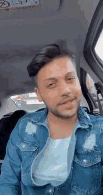 a man is sitting in the back seat of a car wearing a denim jacket and smiling .
