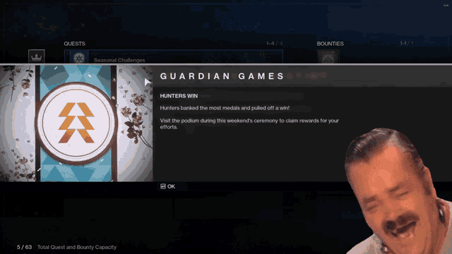 a man is laughing in front of a screen that says " guardian games "