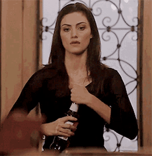 a woman in a black shirt is holding a bottle of wine in her hand .