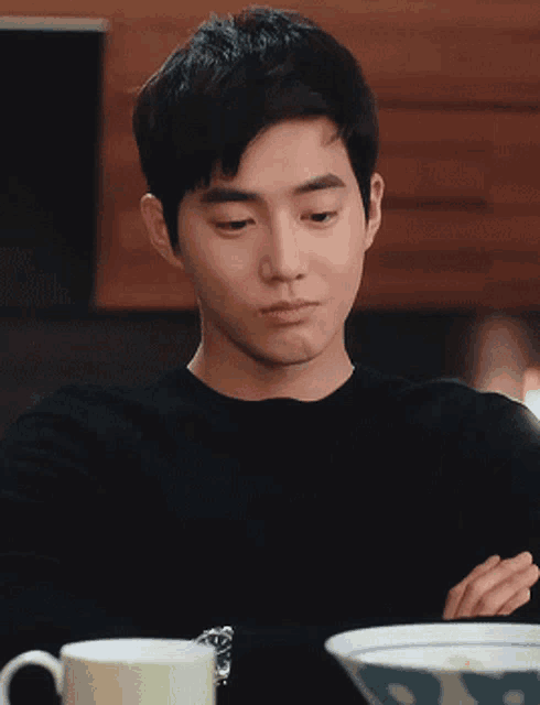 a man in a black shirt is sitting at a table with a bowl of food and a cup of coffee