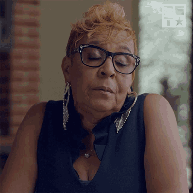 a woman wearing glasses and earrings is sitting in front of a sign that says be t
