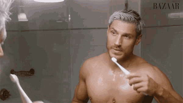 a shirtless man brushing his teeth in front of a mirror with the word bazaar on it