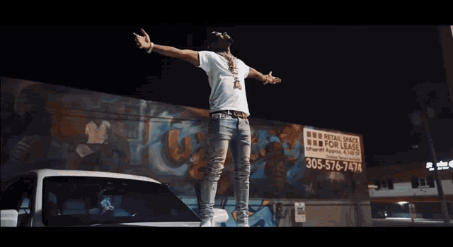 a man is standing on the hood of a truck with his arms outstretched in front of a graffiti wall