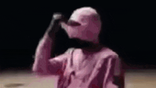 a person wearing a pink shirt and a pink hat is standing in the dark .