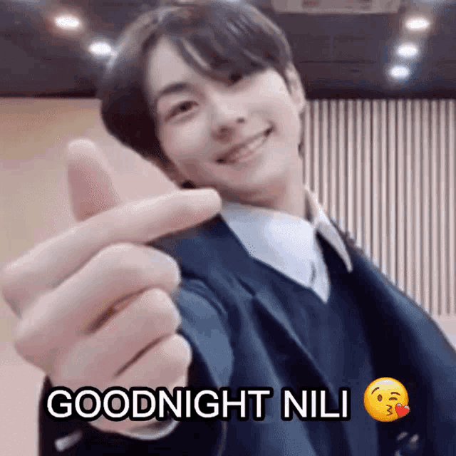 a young man in a suit is making a heart with his fingers and says goodnight nil