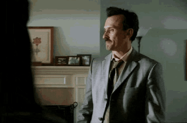 a man in a suit and tie stands in a living room