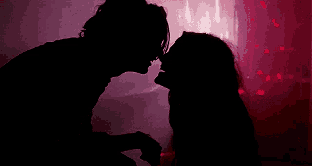 a man and a woman are kissing in the dark in front of a red background .