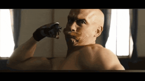 a bald man with a mustache shaving his face with a razor