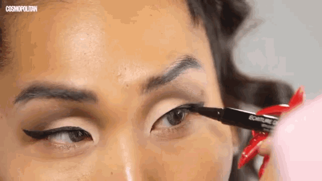 a close up of a woman applying eyeliner with the words cosmopolitan in the background