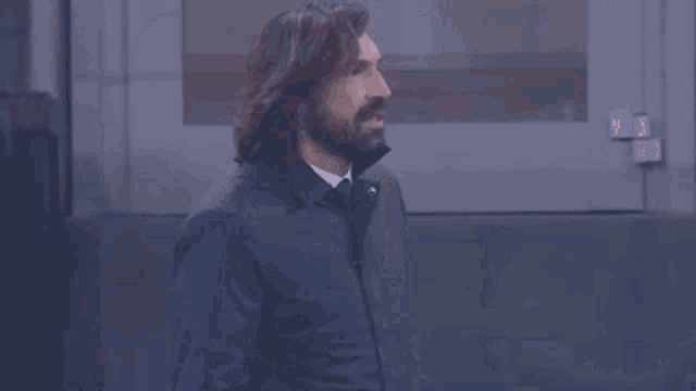 a man with long hair and a beard wearing a blue jacket and tie .