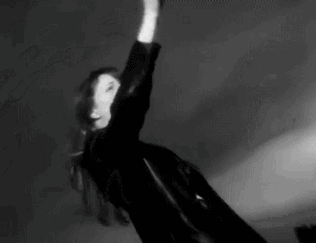 a black and white photo of a woman dancing in a dark room with her arms in the air .