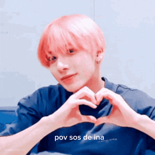 a man with pink hair is making a heart with his hands .