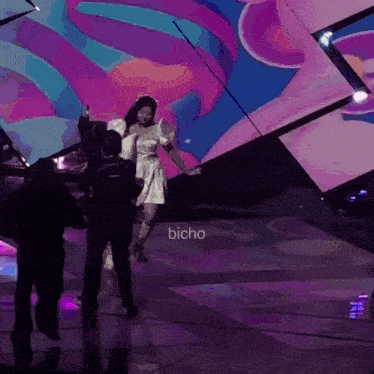 a woman in a white dress is dancing on a stage with bicho written in the lower right corner