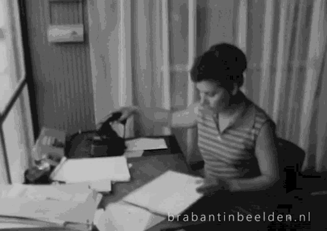 a black and white photo of a woman sitting at a desk with brabantinbeelden.nl written in the corner
