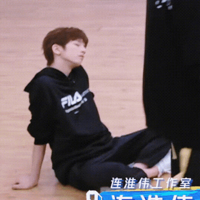 a young man wearing a fila hoodie sits on the floor