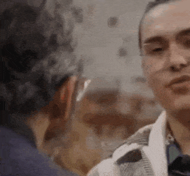 a man wearing glasses is talking to another man in a blurry photo .