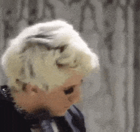 a close up of a person 's head with blonde hair and a black jacket .