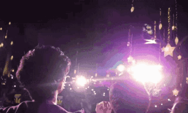 a man stands in front of a stage with purple lights and stars hanging from the ceiling