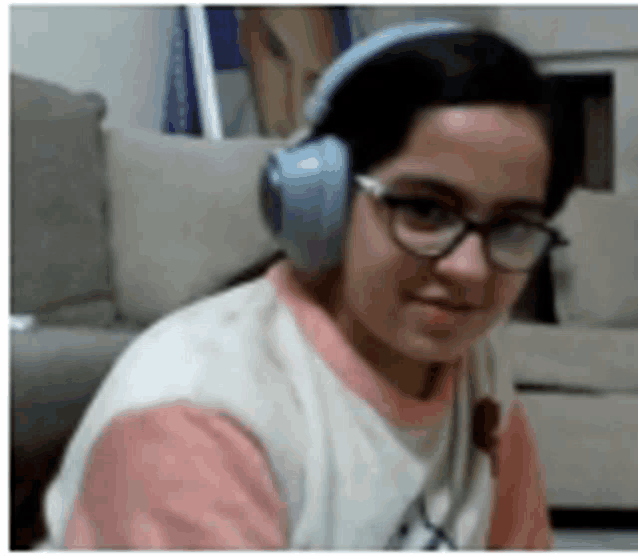 a young girl wearing headphones and glasses is sitting on a couch .