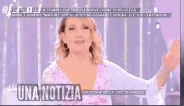 a woman is standing in front of a purple background and talking on a television show .