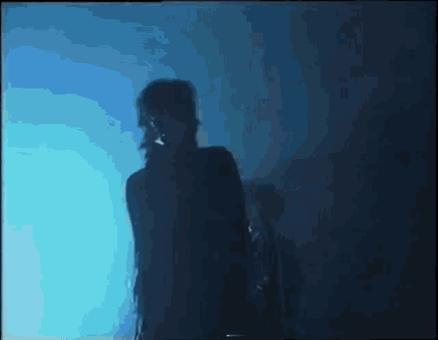 a man in a black suit is standing in a dark room in front of a blue light .