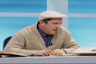 a man wearing a hat and sweater is sitting at a desk .