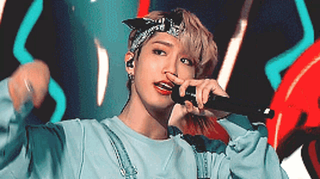 a young man wearing a bandana is singing into a microphone .
