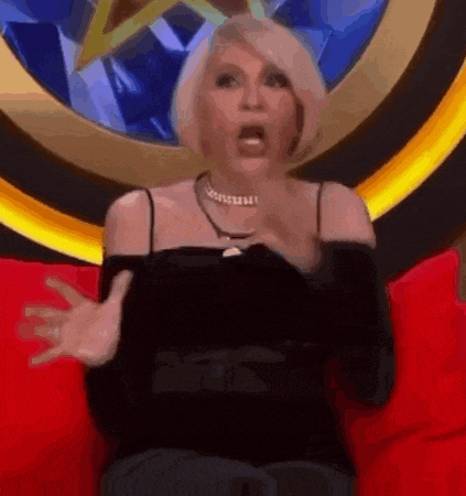 a woman in a black top is sitting on a red couch and making a funny face .