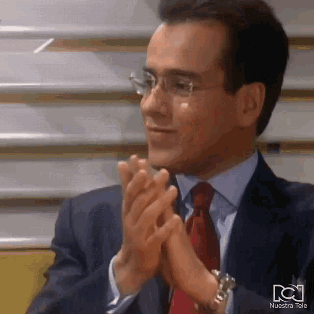 a man in a suit and tie is clapping his hands in front of a nuestra tele logo