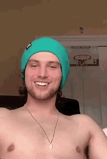 a shirtless man wearing a green hat and necklace is smiling .