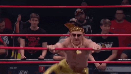 a wrestler wearing a crown and sunglasses is holding a rope in a ring .