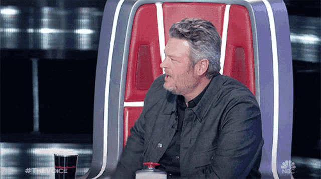 a man sits in a chair with a nbc logo on the back