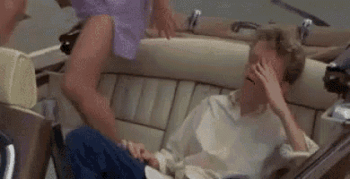 a man is sitting in the back seat of a convertible car covering his face with his hand .