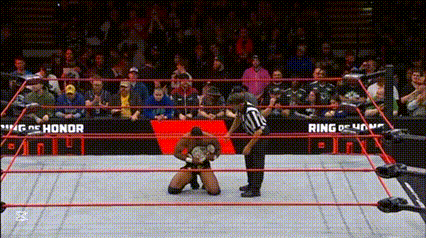 a wrestler is kneeling down in a wrestling ring while a referee stands behind him .