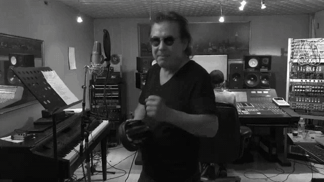 a black and white photo of a man in a recording studio with a microphone and a piano