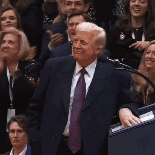a man in a suit and tie is standing in front of a microphone and applauding