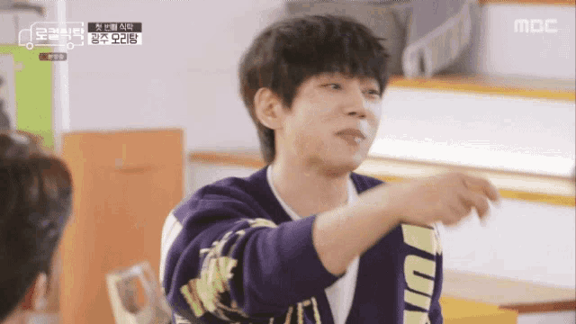 a man in a purple sweater is pointing at something in front of a mbc logo