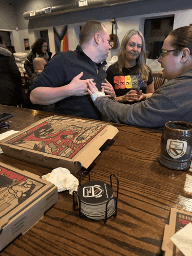 a group of people are sitting at a table with pizza boxes and coasters with a shield on them