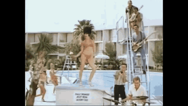 a woman in a bikini is standing on a diving board while a band plays behind her
